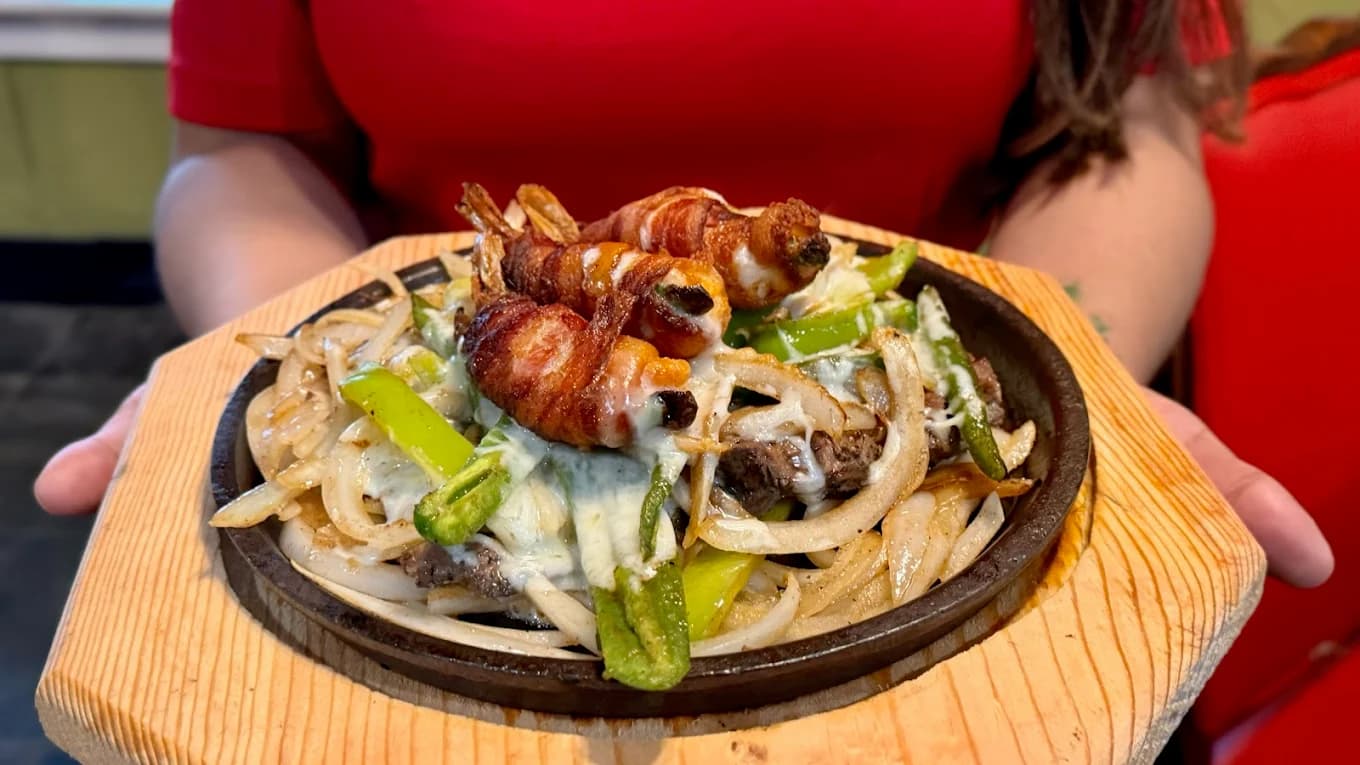 Sizzling beef fajitas with bacon-wrapped shrimp on a hot skillet at Las Piñatas Kitchen Tomball
